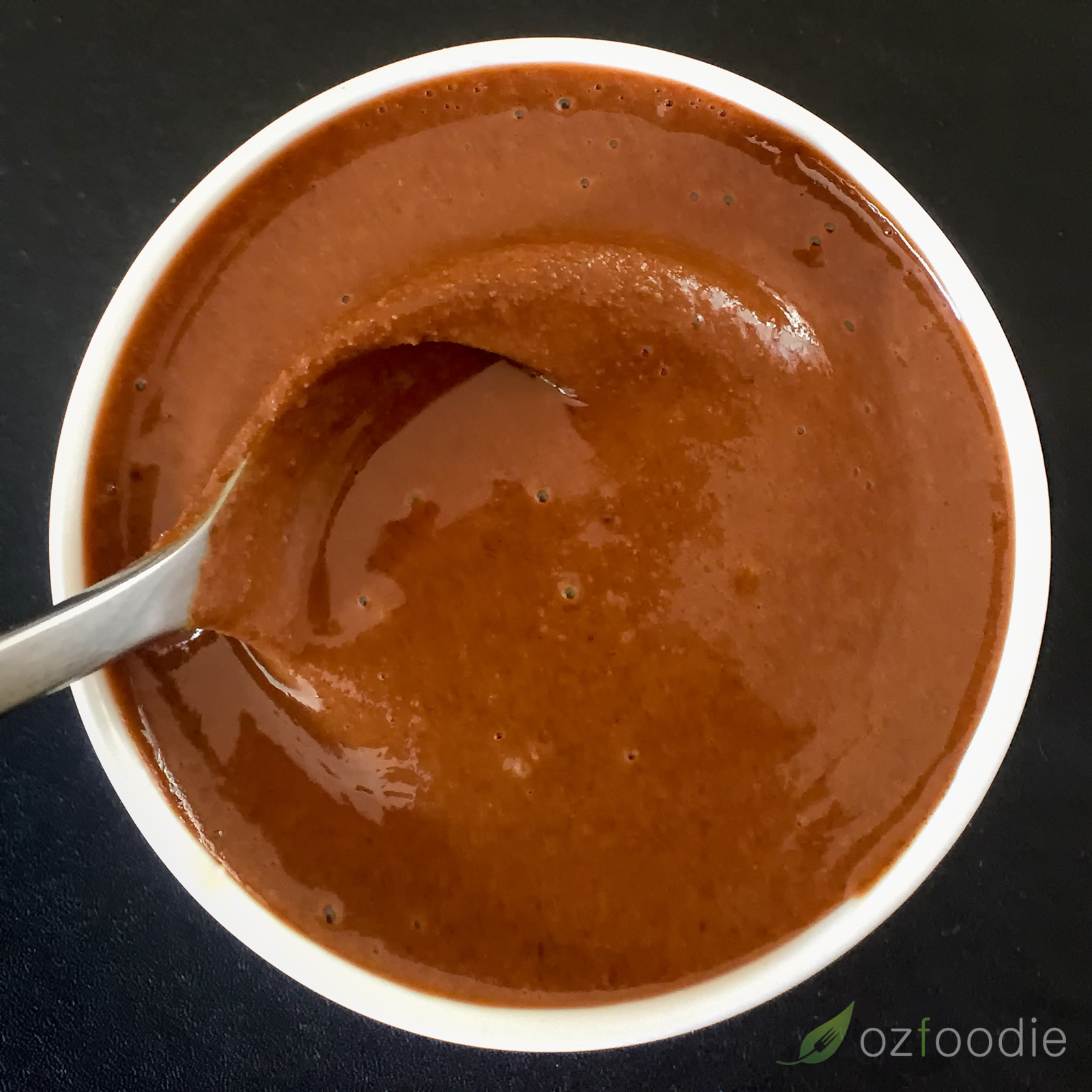 Rich brown roasted almond butter in a white bowl, on a black background.