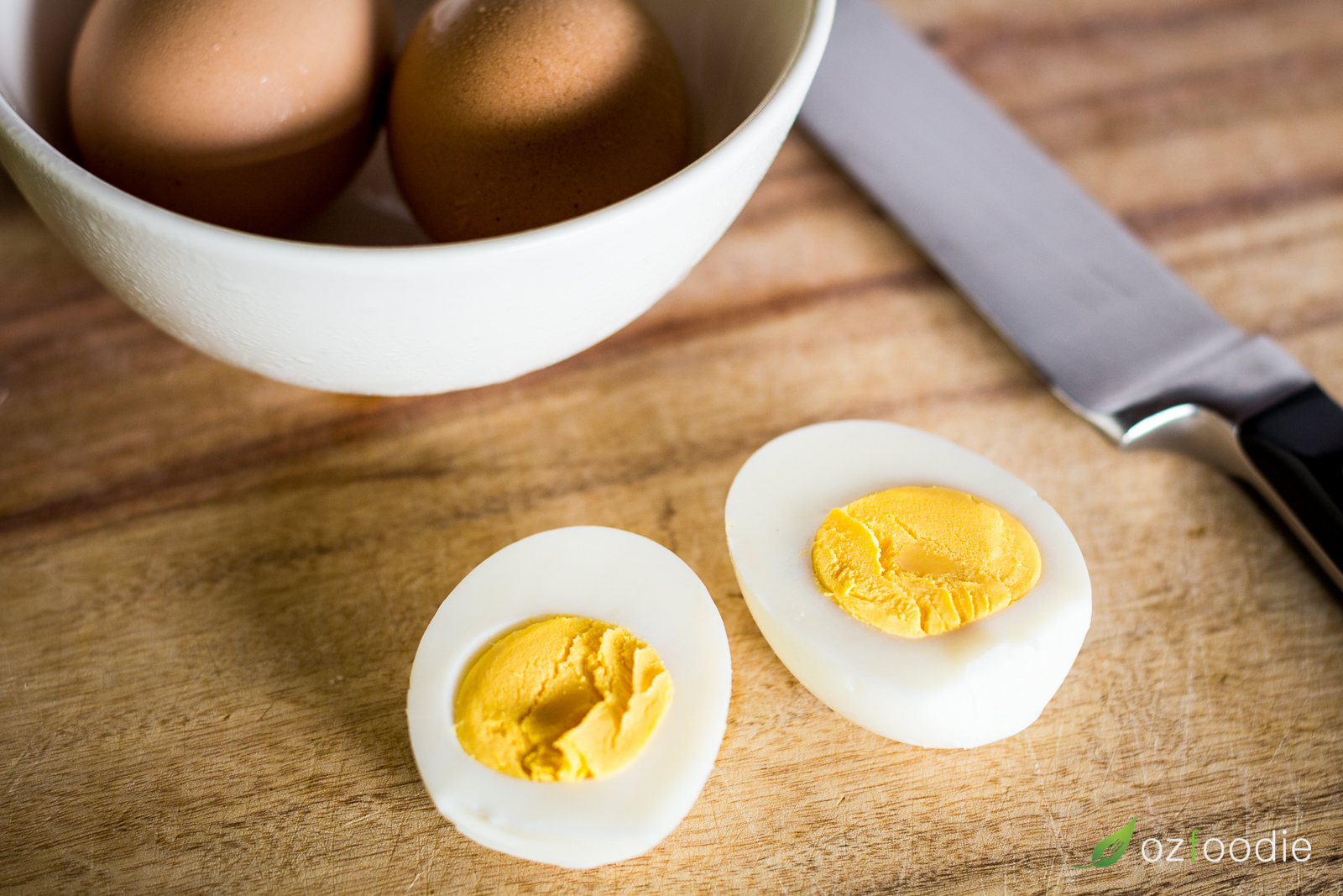 A bowl of hard-boiled eggs with a peeled and halved egg in the foreground.