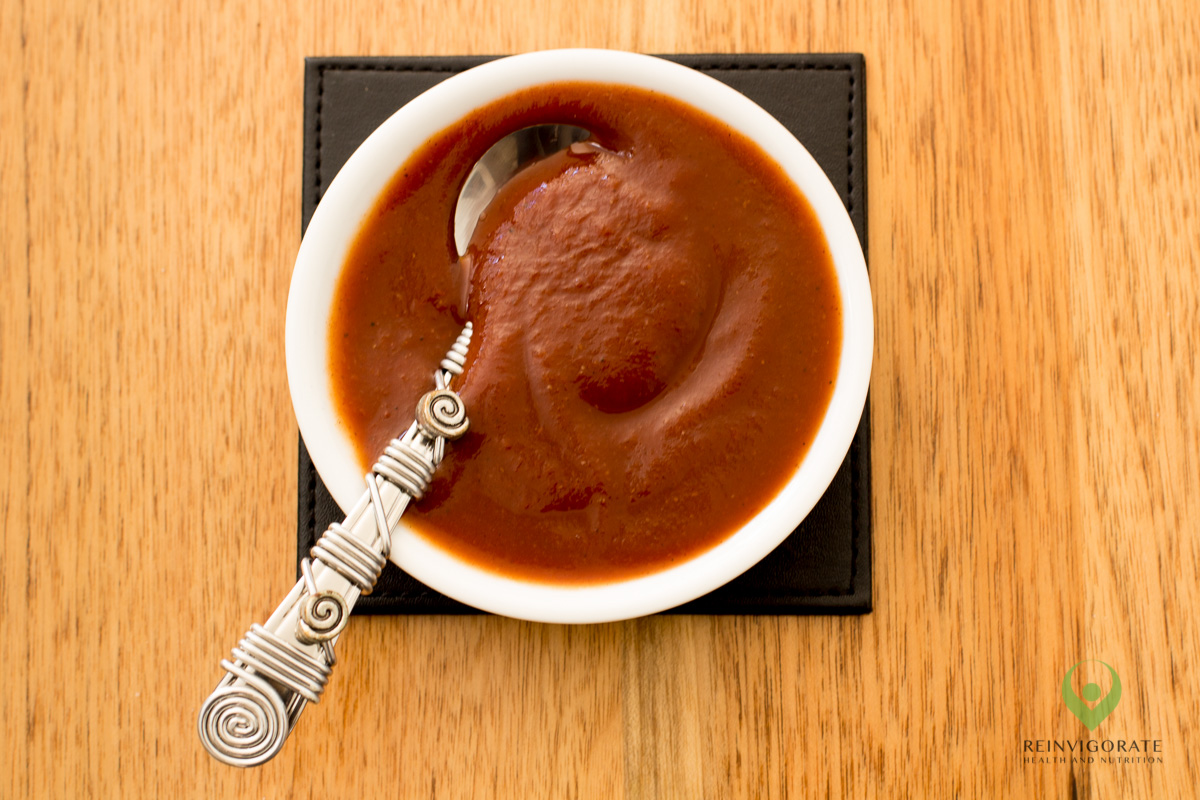 Tomato sauce in a small white dish on a lightly-coloured timber surface.